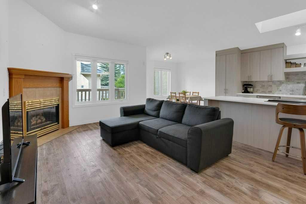 Modern open-plan living room with dark sectional sofa, fireplace, wood flooring, and kitchen bar stools