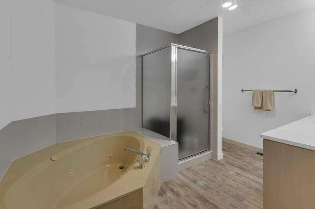 Modern bathroom with beige tub, glass shower, gray walls, and wood-look floor.