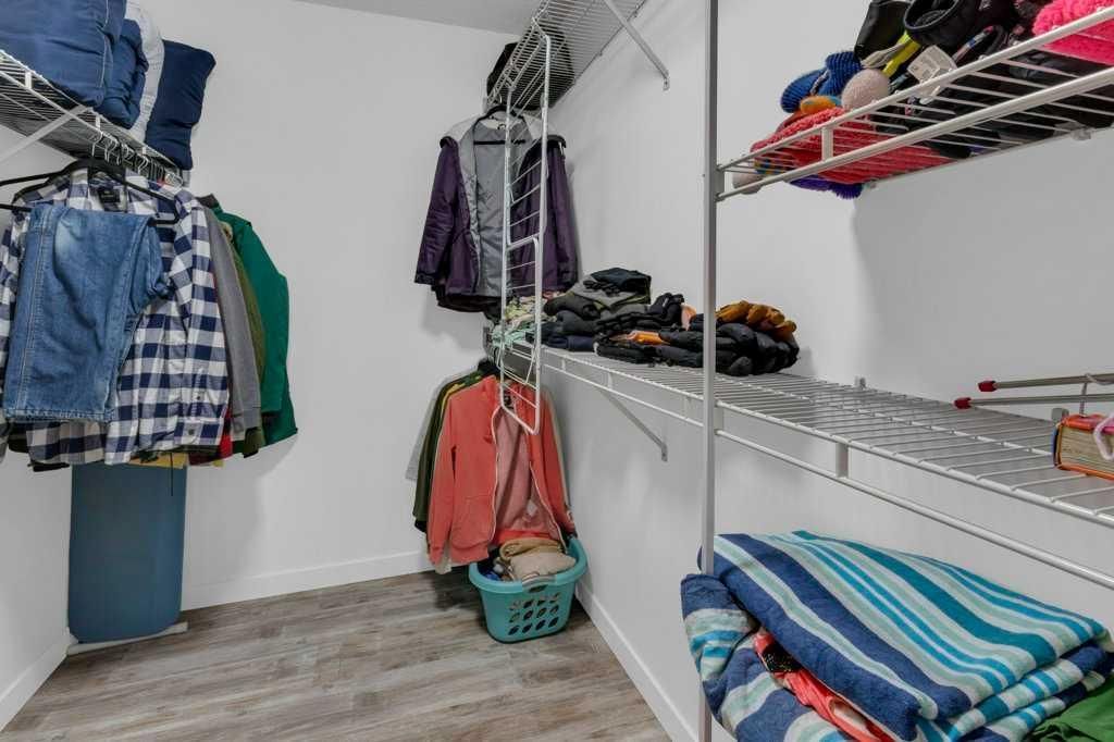 Walk-in closet with hanging clothes, folded sweaters, and shoe shelves on white wire racks.