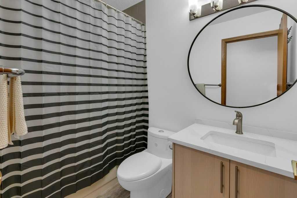 Modern bathroom with striped shower curtain, toilet, vanity sink, and round mirror