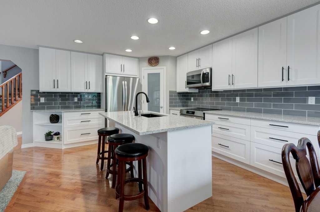 Modern white kitchen with marble island, black bar stools, stainless appliances, and wood floors