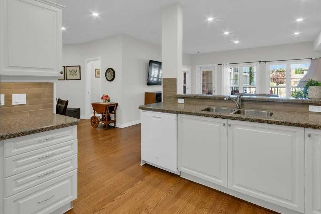 Bright kitchen with white cabinets, granite island, and hardwood floors opening to a dining area.