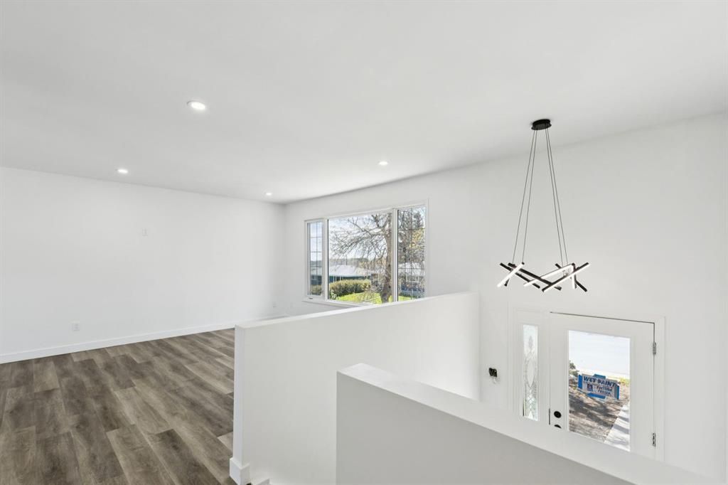 Bright white interior with wood floors, staircase, window, and modern hanging light fixture