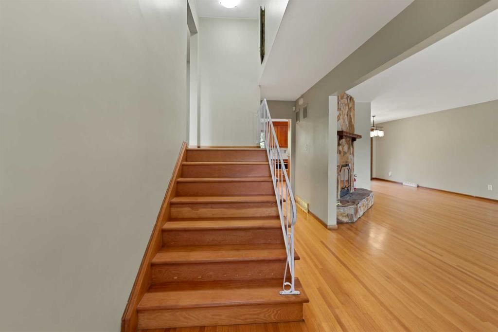 Wooden staircase beside an open living room with hardwood floors and stone accent wall