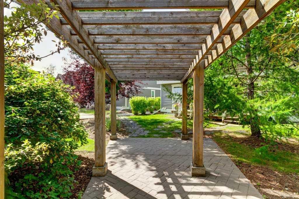 Shaded garden walkway with a wooden pergola, stone path, and lush green plants.