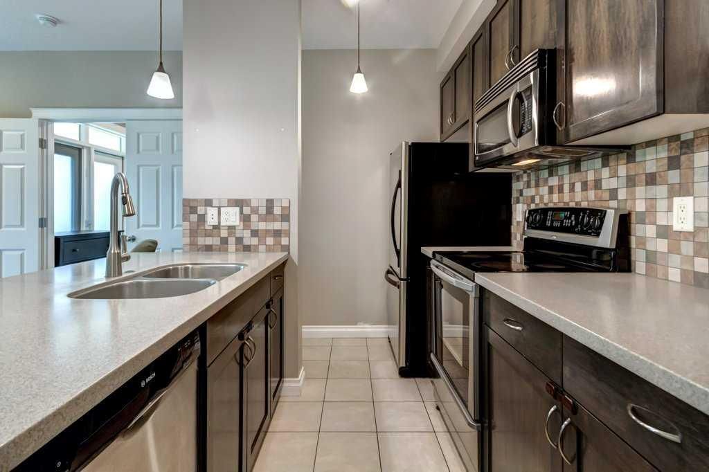 Open-plan kitchen with granite island, three stools, pendant lights, and tiled floor