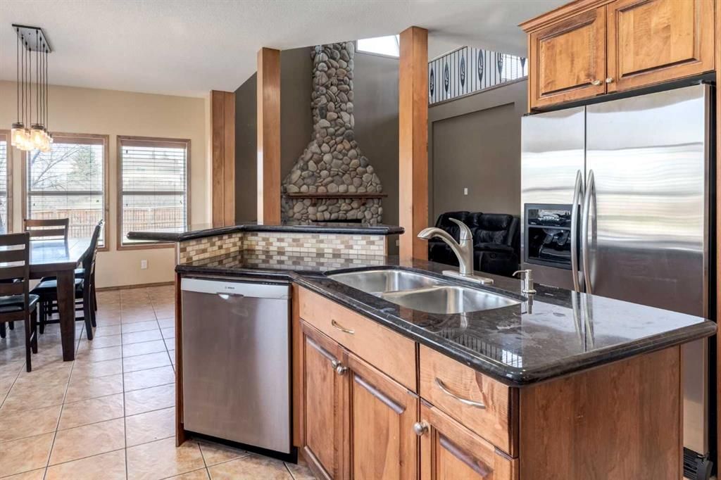Modern kitchen with wood cabinets, granite island, stainless steel fridge, and dining area in background