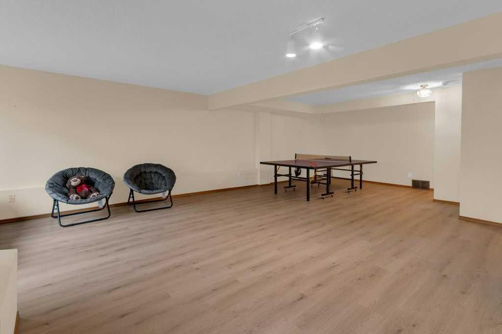 Empty basement rec room with beige walls, wood flooring, two chairs, and a small table