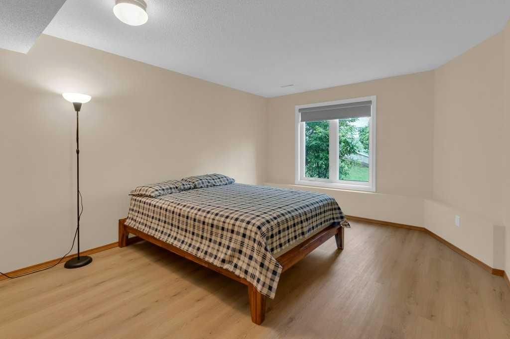 Empty bedroom with a bed, floor lamp, wood floor, and a window showing greenery.