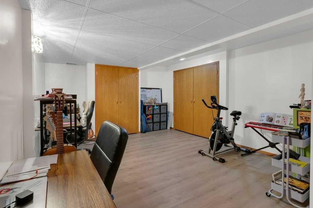 Spacious home gym with exercise bike, shelves, wooden doors, and a desk area under bright white ceiling.