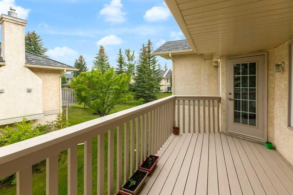 Apartment balcony with beige railings, potted plants, and a view of neighboring homes and trees