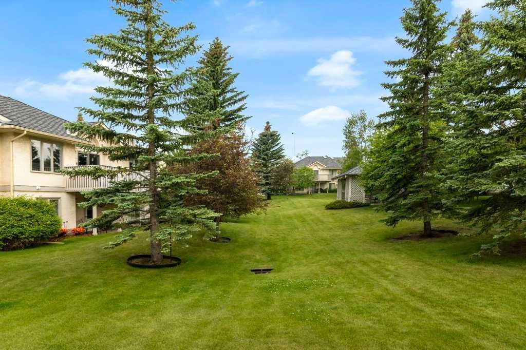 Green lawn with tall trees and a row of houses under a partly cloudy sky