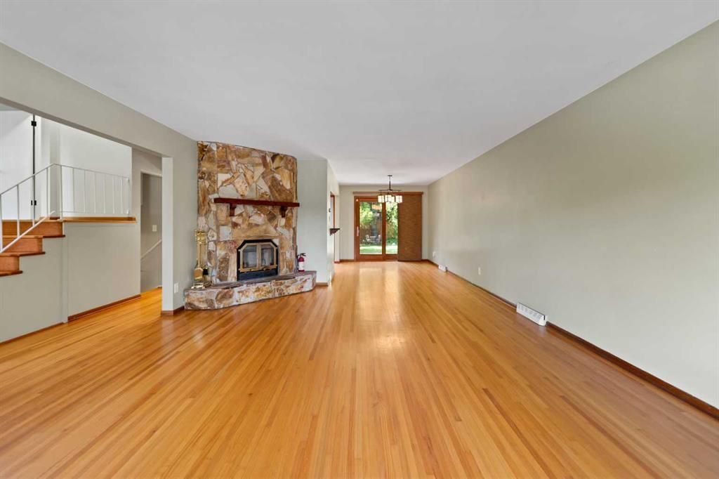 Spacious living room with hardwood floors, stone fireplace, staircase, and large windows