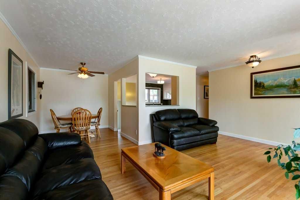 Bright living room with black leather sofas, wooden coffee table, dining area, and wall art