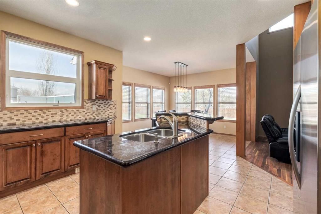 Spacious kitchen with wood cabinets, granite island, tile floor, and bright windows.