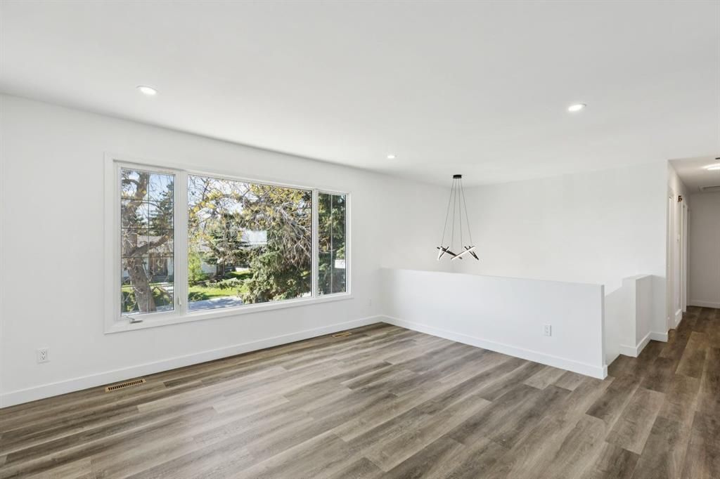 Bright empty living room with large window, gray wood floors, and white walls