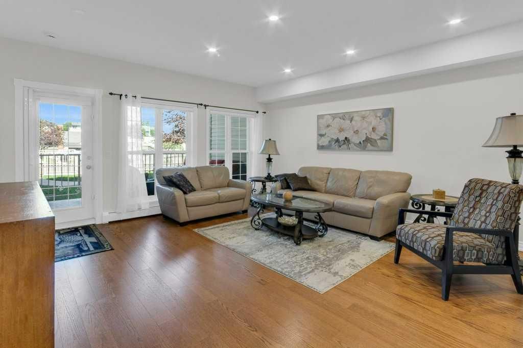Bright living room with beige sofas, armchair, rug, wooden floor, and large windows.