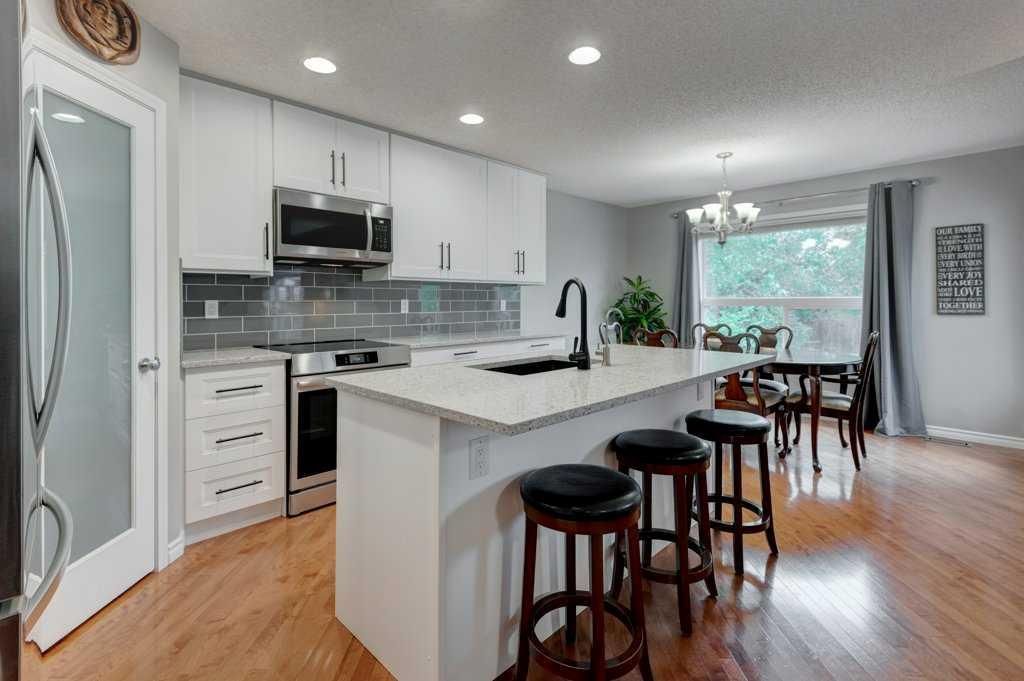 Bright modern kitchen with white cabinets, island seating, and a dining area by a window