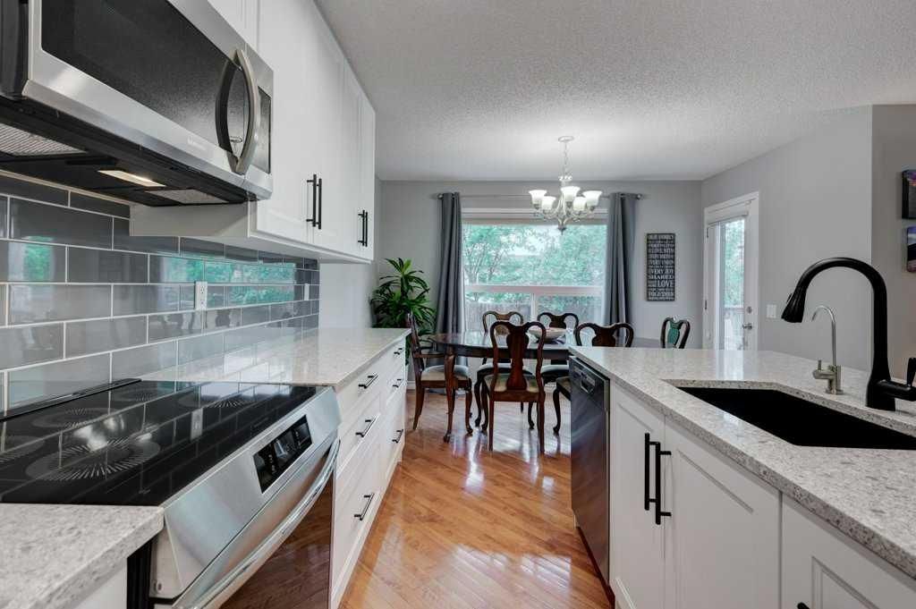Modern white kitchen with stainless appliances, black countertops, and dining area by a bright window.