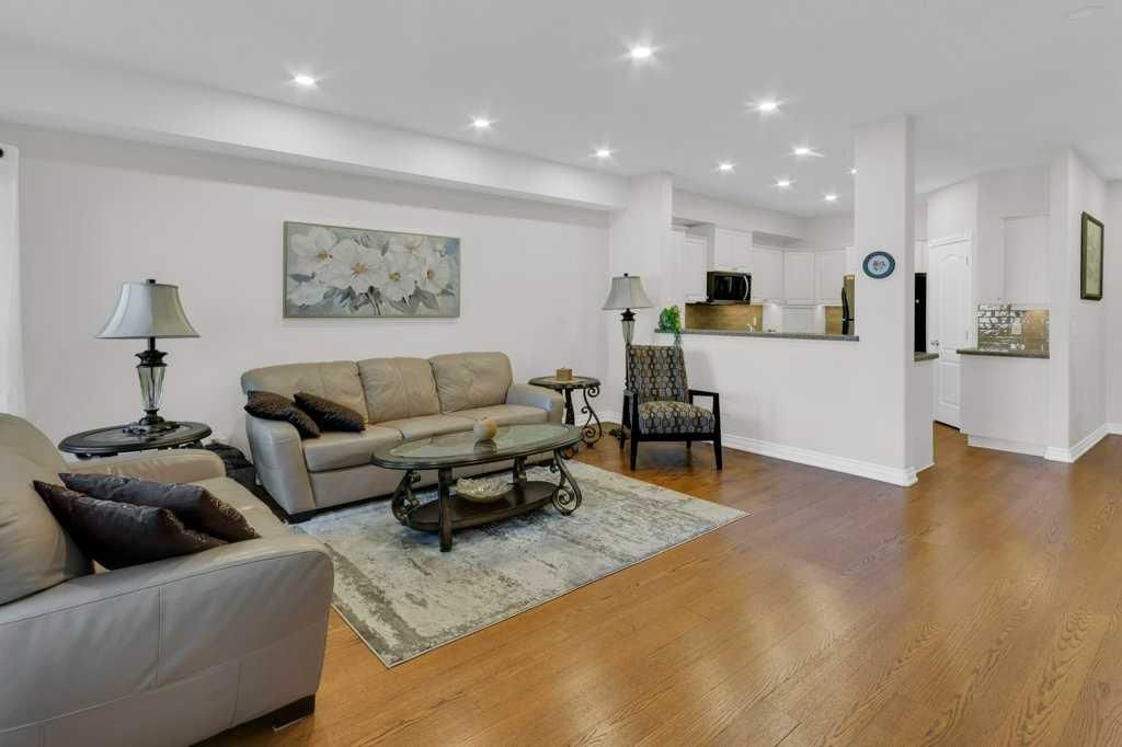 Bright modern living room with beige sofas, wood floors, patterned rug, and open kitchen area