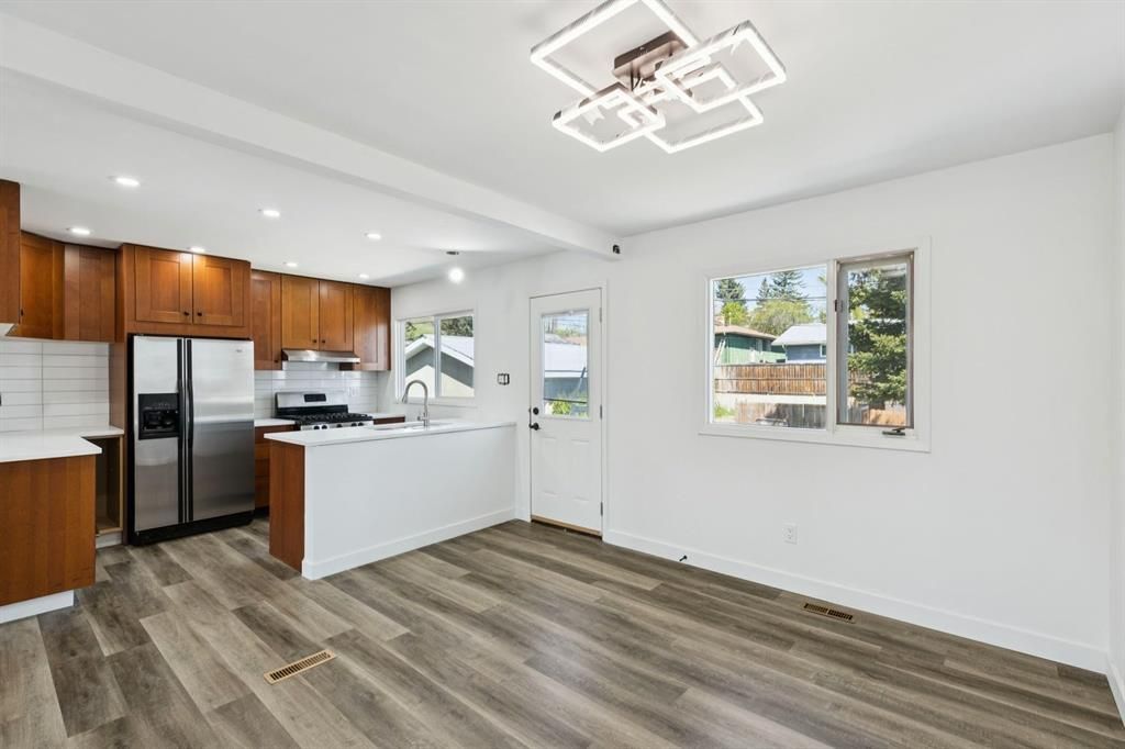 Bright modern kitchen with wood cabinets, stainless fridge, white island, and large window over wood-look flooring