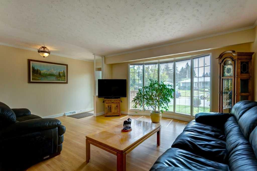 Bright living room with black sofas, wooden coffee table, TV, potted plant, and large windows overlooking greenery