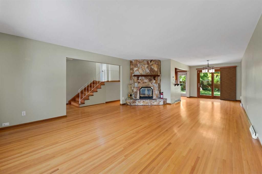 Empty living room with hardwood floors, fireplace, stairs, and large windows overlooking a yard