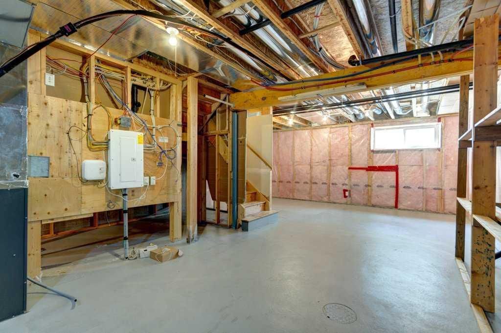 Unfinished basement with exposed insulation, wiring, and concrete floor, lit by daylight from small windows.