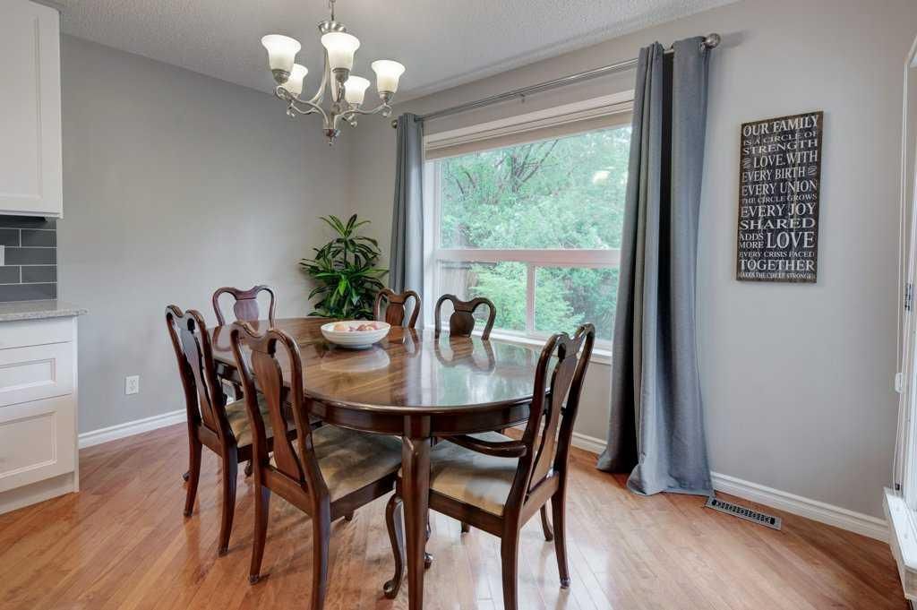 Dining room with a round wooden table, chairs, chandelier, and large window with gray curtains.