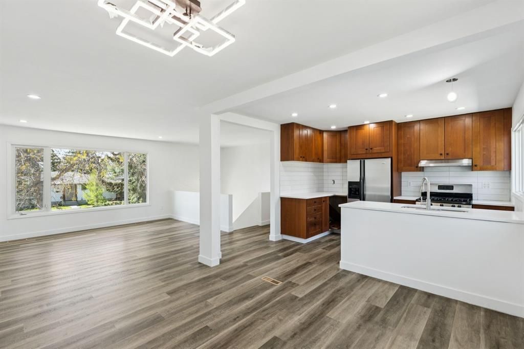 Bright open kitchen and dining area with wood cabinets, white island, gray floors, and large window