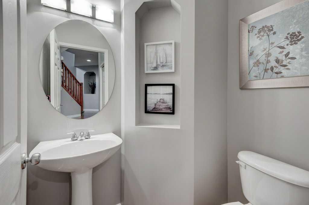 Small white bathroom with pedestal sink, round mirror, toilet, and wall art.