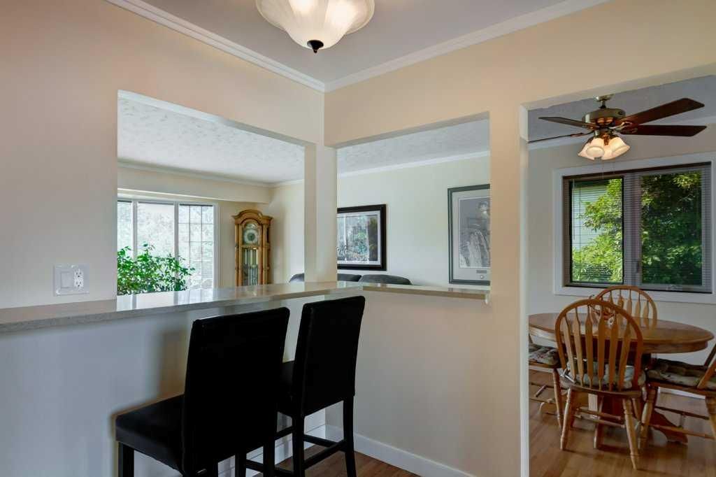 Bright dining area with black bar stools, open pass-through, and a glimpse of a ceiling-fan lit patio beyond.