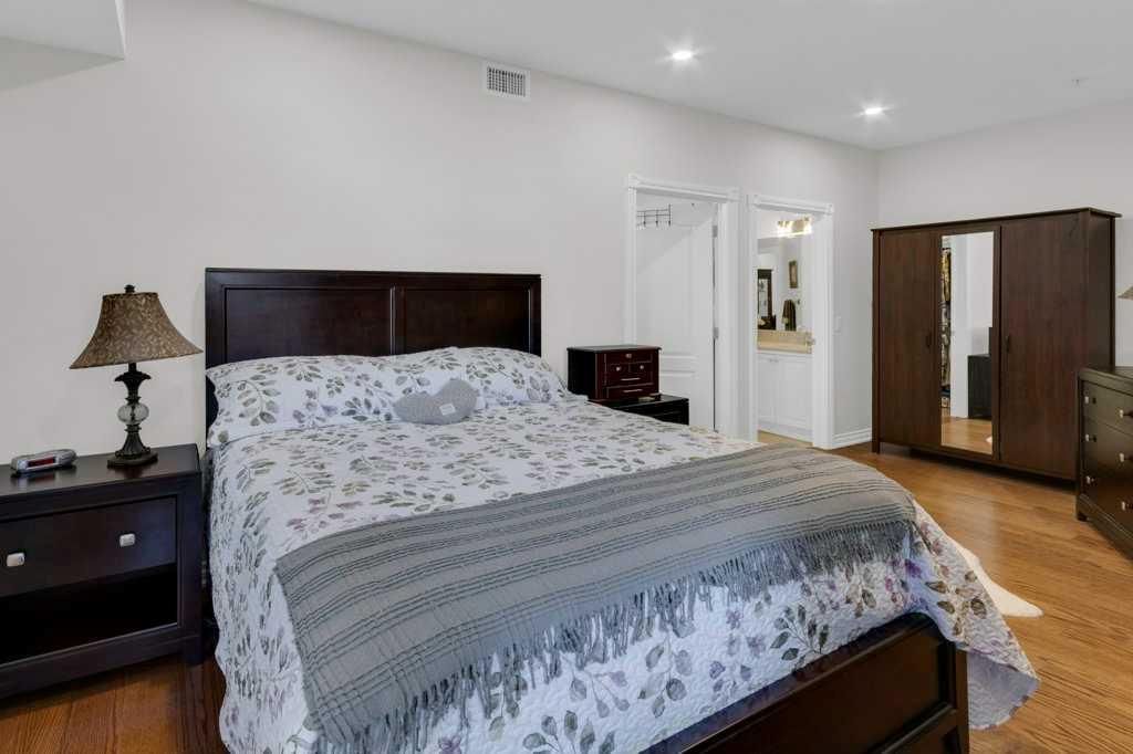 Spacious bedroom with a made bed, dark wood furniture, white walls, and hardwood floor.