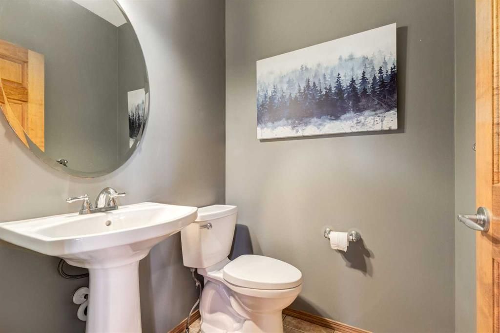Small bathroom with pedestal sink, toilet, round mirror, and forest landscape wall art.