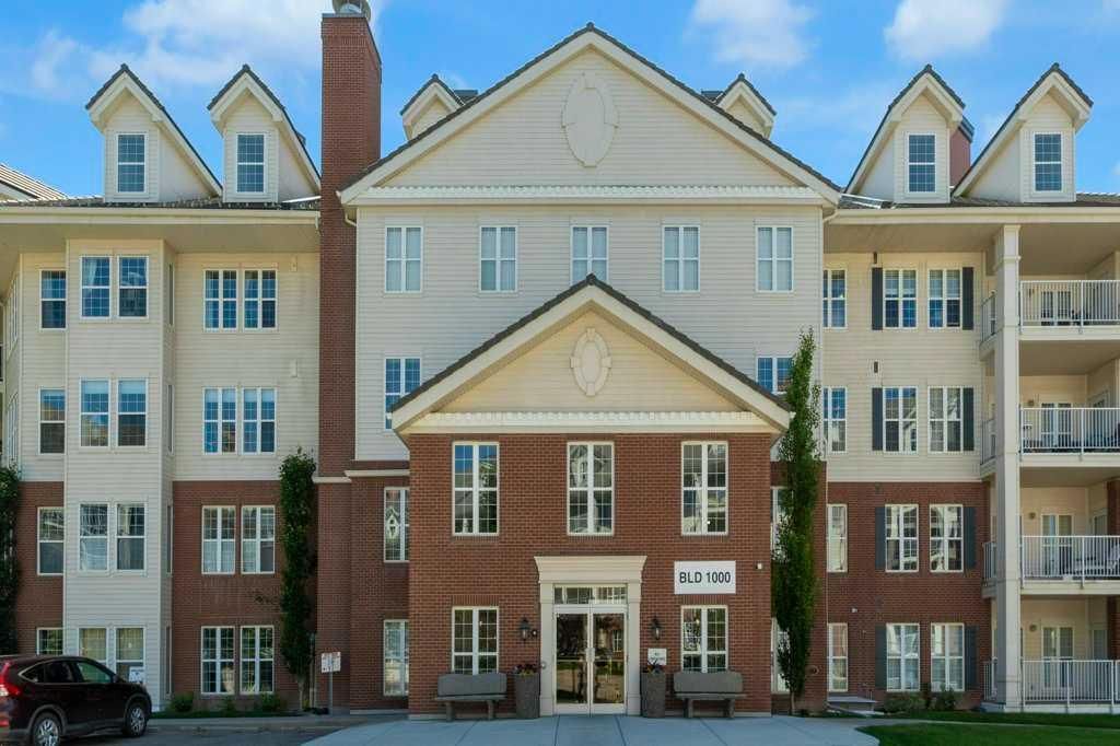 Apartment building with brick and beige siding, white balconies, and a central entrance under blue sky