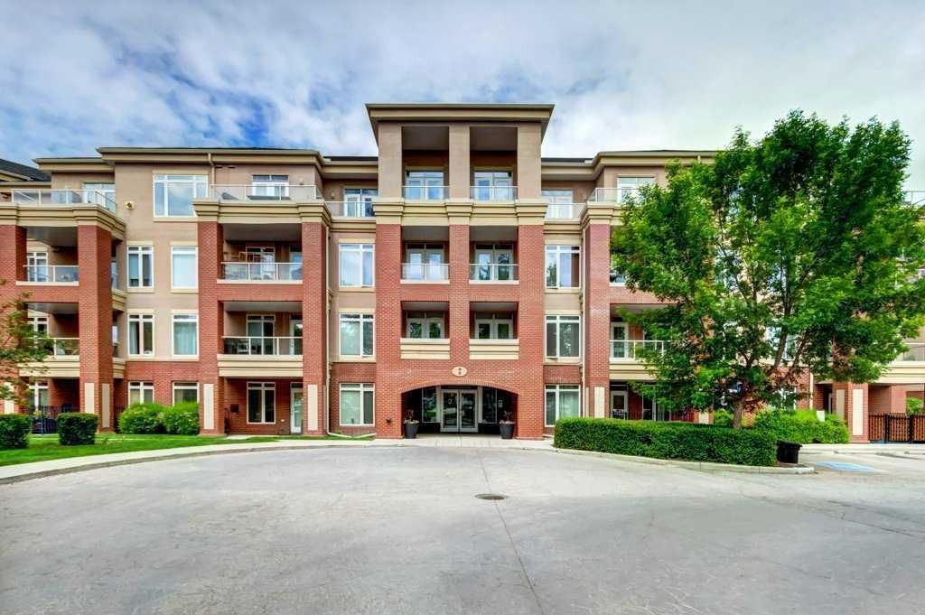 Brick apartment building with balconies and a tree-lined entrance drive