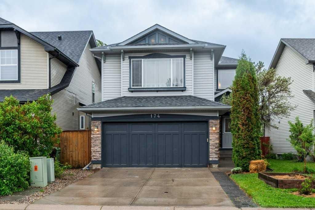 Two-story gray house with a dark garage door and wet driveway on a cloudy day