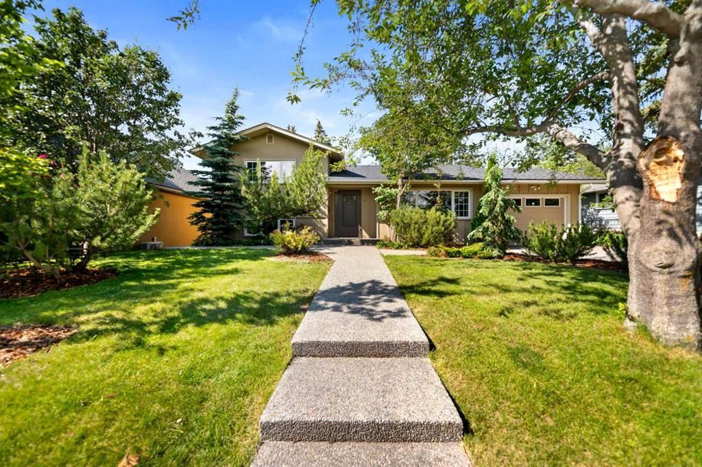 Front walkway leading to a house with a green lawn, trees, and bright sunlight