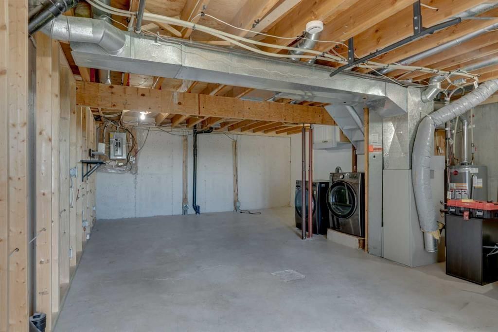 Unfinished basement with exposed ductwork, wood joists, concrete floor, and utility equipment along the wall