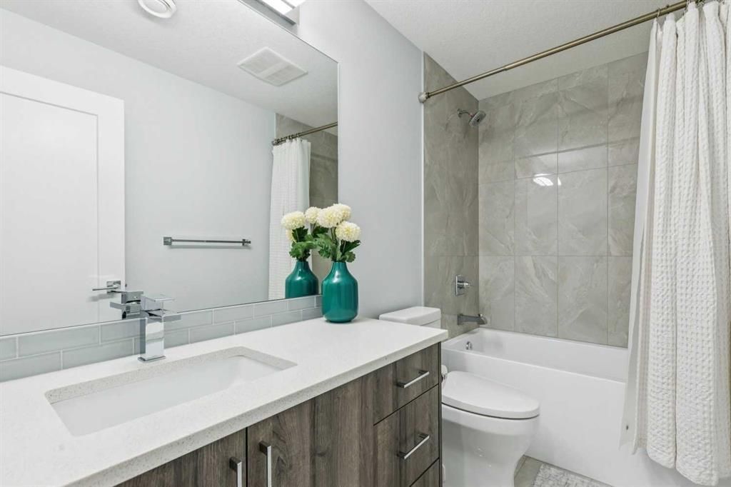 Modern bathroom with double vanity, large mirror, white tub, and teal vases with flowers