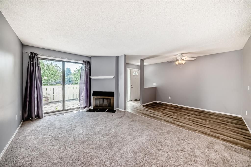 Spacious empty living room with gray walls, carpet, sliding glass doors, and a fireplace.