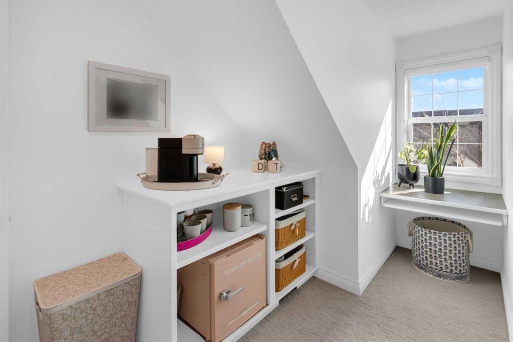 Bright white attic room with shelves, storage bins, a window seat, and a small wicker stool