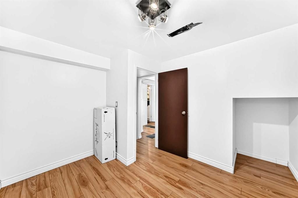 Empty white room with hardwood floors, ceiling fan, open door, and wall niche
