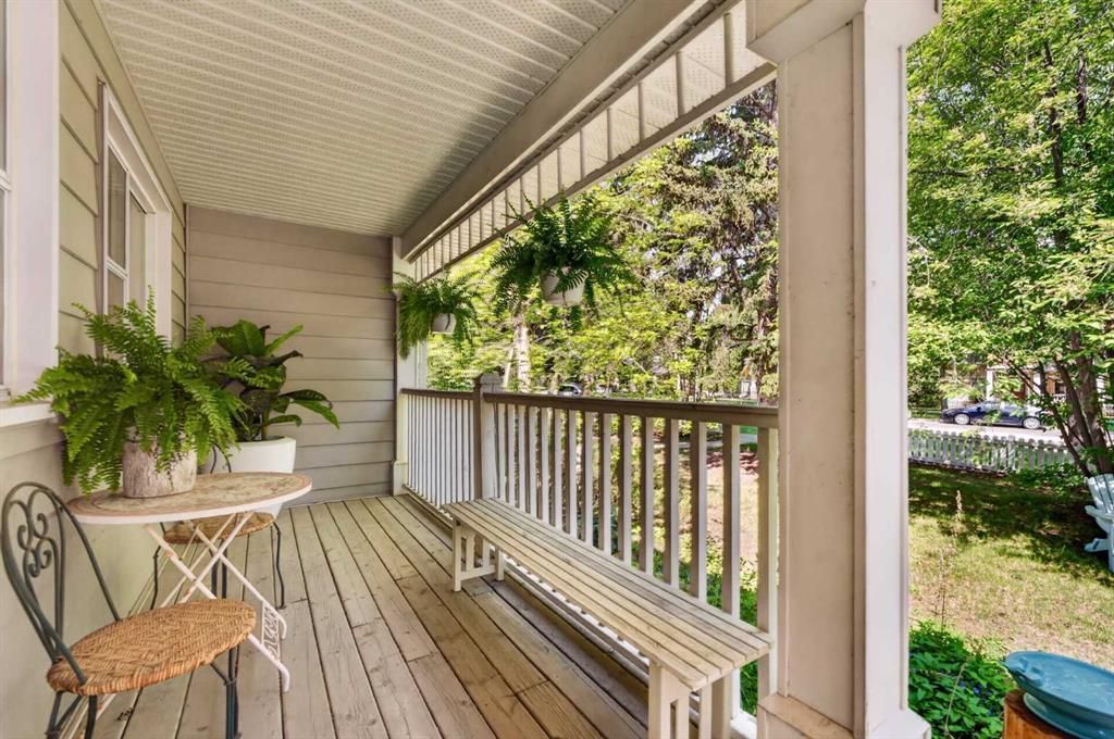 Covered front porch with white railing, bench, and potted plants overlooking a leafy yard