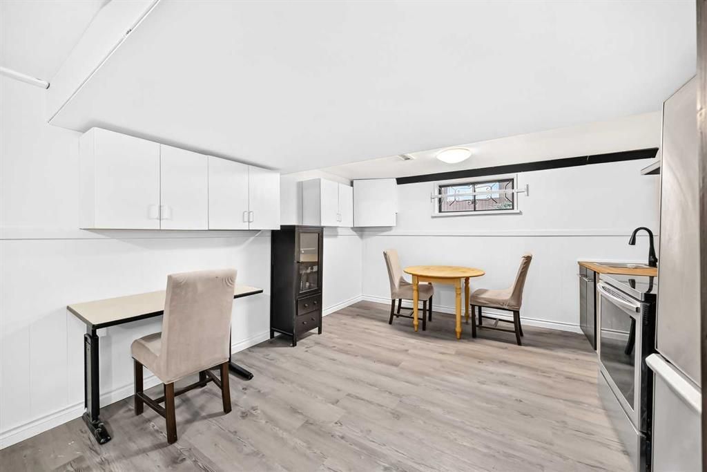 Bright kitchen-dining area with white cabinets, wood floors, a small table, chairs, and a desk by the wall