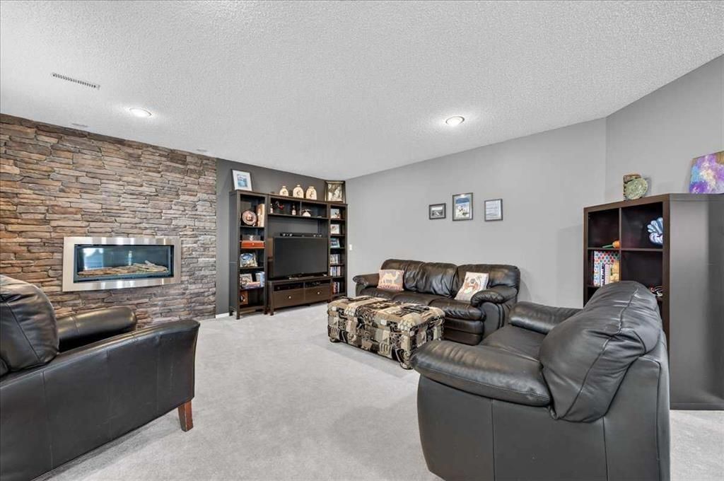 Living room with stone accent wall, black leather chairs, patterned sofa, and built-in shelves