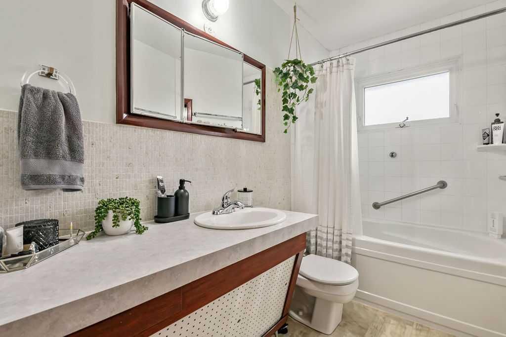 Bright bathroom with white tub, wooden vanity, mirror, and potted plants