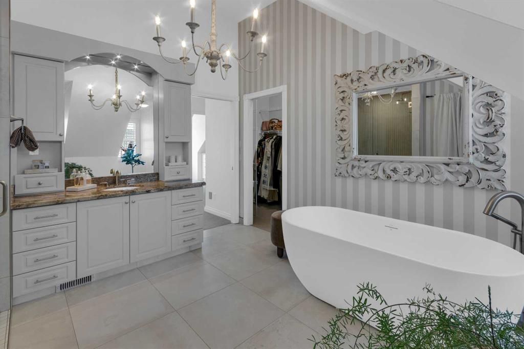 Bright white bathroom with double vanity, ornate mirror, chandelier, and freestanding tub