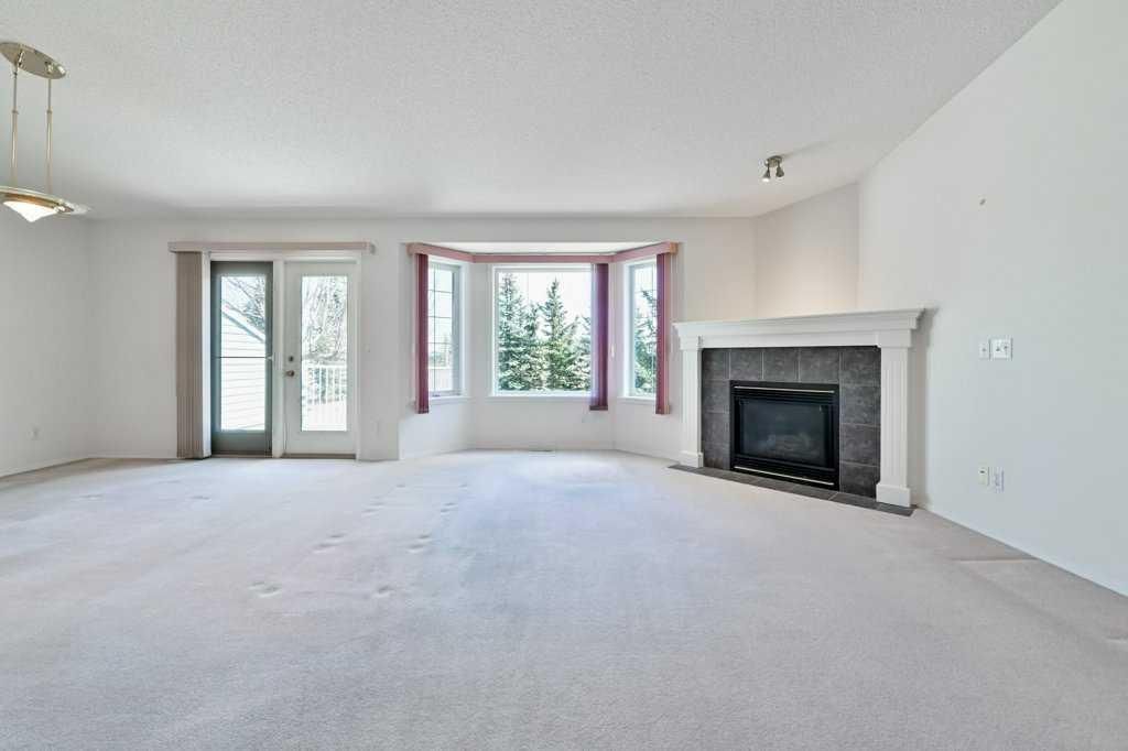 Empty living room with white walls, beige carpet, large windows, and a fireplace