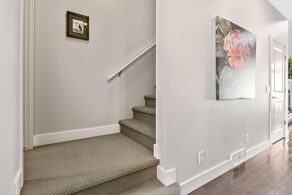 Interior hallway with carpeted stairs, white walls, hardwood floor, and wall art.
